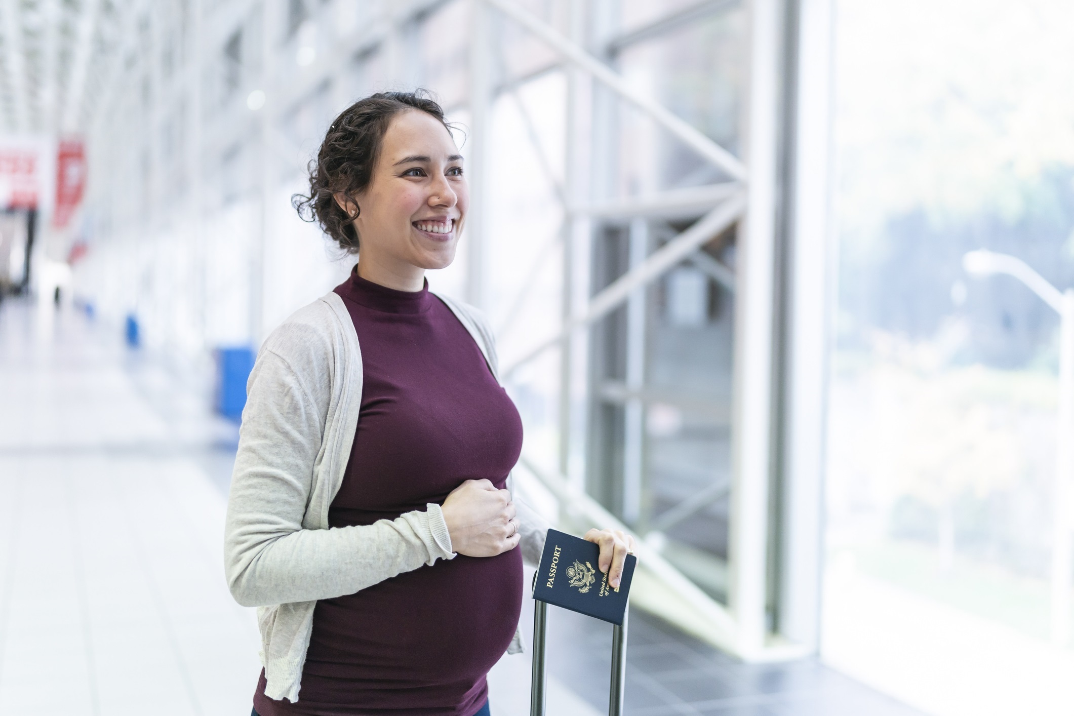 Ein schwangeres Mädchen lächelt am Flughafen mit ihrem Reisetrolley