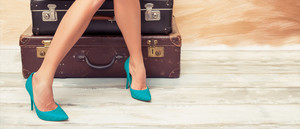 Woman's legs with turquoise shoes sitting on stacked suitcases