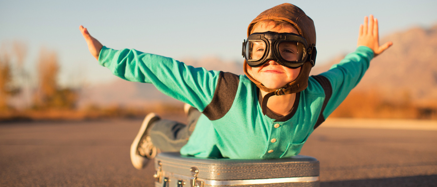 Bambino vestito da aviatore simula di volare sdraiato su una valigia