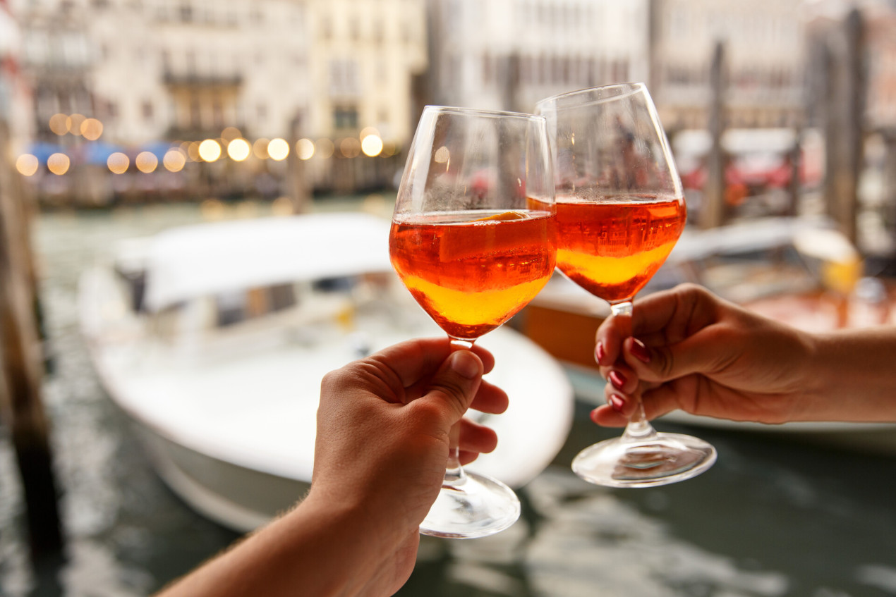 Hands toasting with glasses of spritz, with Venetian canal in the background