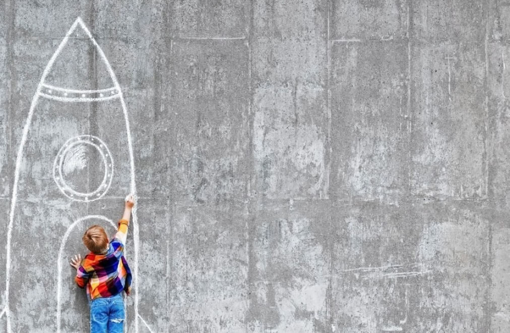 Bambino disegna con un gesso un razzo su una parete