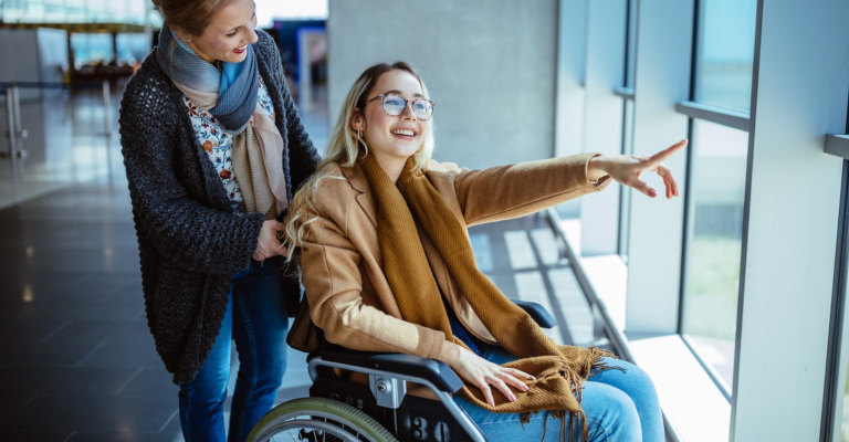 Young disabled woman on wheelchair with her companion smile in an airport looking out.