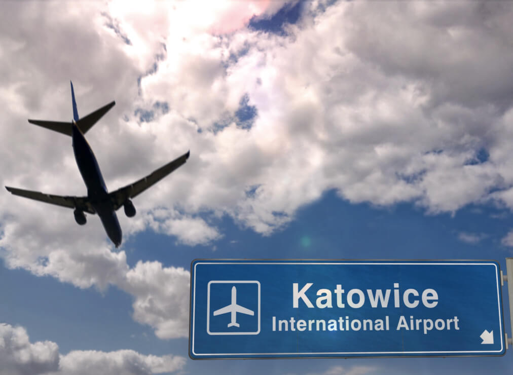 Katowice International Airport sign with plane taking off in the background.